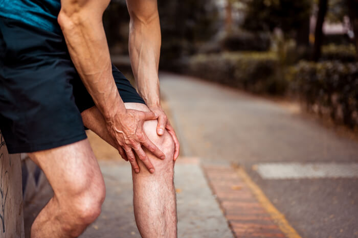 Bent-over person in shorts holding aching knee.